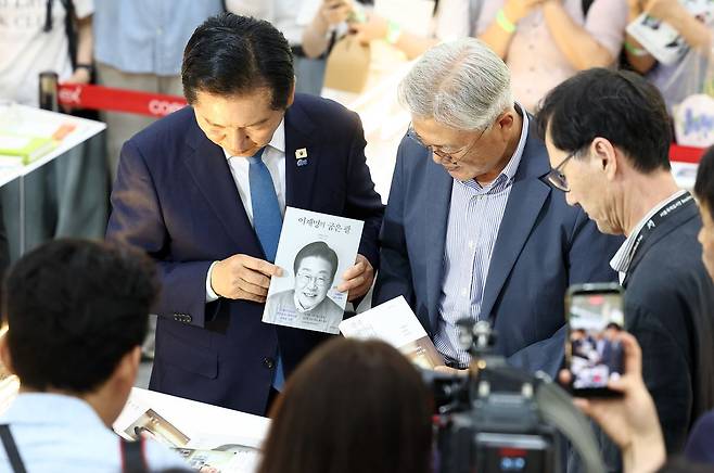 정청래 전 민주당 대표가 24일 코엑스에서 열린 서울국제도서전 ‘돌베개·평산책방’ 부스를 찾아 문재인 전 대통령과 인사하고 이재명 대통령의 저서를 들어 보이고 있다. 뉴스1