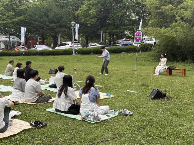 지난 21일 오후 경남 도민의 집 인근 잔디밭에서 관객들이 창원시민뮤지컬단의 버스킹형 뮤지컬 ‘버스정류장’을 관람하고 있다.