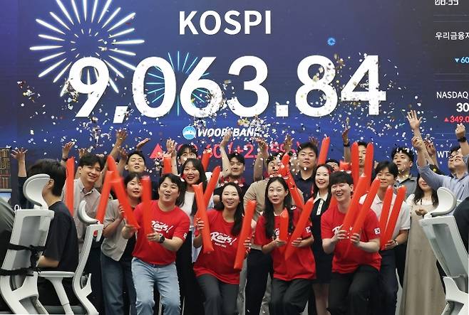 코스피 지수가 전인미답의 9000선 고지를 돌파한 18일 오후 서울 중구 우리은행 본점 딜링룸에서 직원들이 코스피 종가를 배경으로 축하 세리머니를 하고 있다. 코스피는 이날 전일 대비 199.60포인트(2.25%) 오른 9063.84에 장을 마쳤다. 2026.6.18 뉴스1