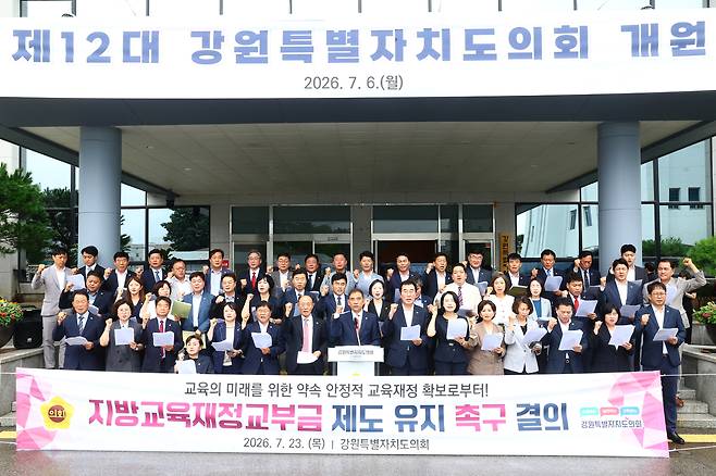 강원도의회 여야의원들이 모두 의회 현관에 모여, 학령인구 감소를 이유로 지방교육제정교부금을 줄이려는 중앙정부의 최근 움직임에 대해 비판하며 현행 유지를 촉구하고 있다.