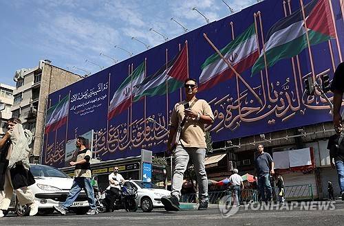 이란 테헤란의 한 거리에서 시민들이 이란과 팔레스타인 국기가 그려진 대형 광고판 앞을 지나가고 있다. [EPA 연합뉴스. 재판매 및 DB 금지]