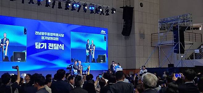 15일 전남광주통합특별시 나주시 종합스포츠파크 다목적체육관에서 열린 '전남광주통합특별시당 정기 당원대회'에서 초대 시당 위원장으로 선출된 안도걸 국회의원(무대 위 왼쪽)이 양부남 광주시당 위원장으로부터 당기를 인수받고 있다. 황태종 기자