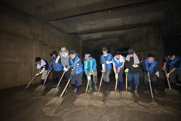 수해를 입은 지하 시설에서 '바르게살기운동 옥포1동위원회' 봉사자들이 일렬로 늘어서서 바닥에 쌓인 두꺼운 토사를 치우고 있다.
