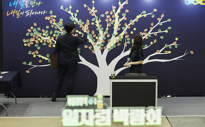 지난 9월 8일 부산 해운대구 벡스코 제2전시장 ‘부·울·경 광역이음 일자리박람회’에 마련된 ‘함께 채우는 내일의 소원나무’에 한 구직자가 취업을 바라는 마음을 담은 메모를 붙이고 있다. 연합뉴스