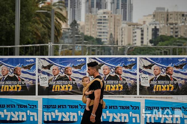[텔아비브=AP/뉴시스] 이스라엘 총선이 치러진 27일 텔아비브에서 아이를 안은 한 남성이 리쿠드당 선거 벽보 앞을 지나고 있다. 베냐민 네타냐후 총리가 자신의 지지를 선언한 도널드 트럼프 미국 대통령과 함께 등장했다. 2026.10.28.