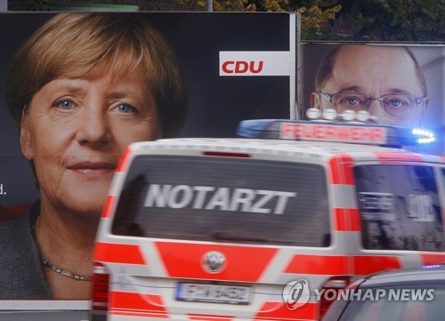 An ambulance drives by election posters of German Chancellor Angela Merkel, left, and her challenger Martin Schulz from the Social Democrats in Frankfurt, Germany, Wednesday, Sept. 20, 2017. German elections will be held on upcoming Sunday. (AP Photo/Michael Probst)