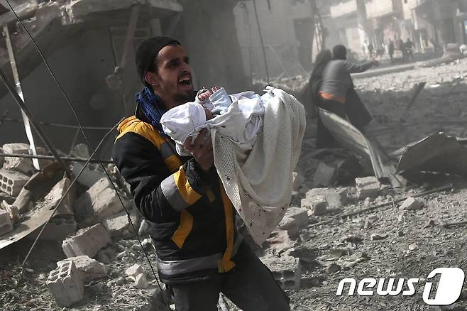 19일(현지시간) 시리아 동구타 지역에서 한 남성이 시리아 정부군의 공습으로 다친 아기를 안고 뛰고 있다.  © AFP=뉴스1