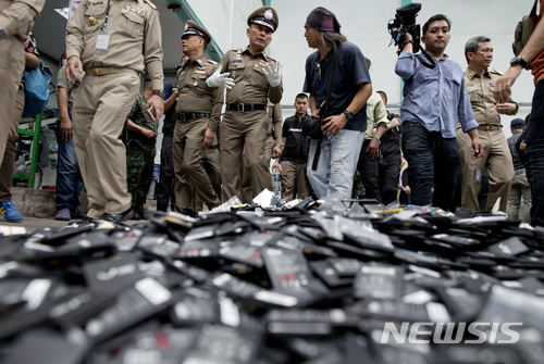 【방콕(태국)=AP/뉴시스】위라차이 송메타 태국 경찰청 차장(가운데)이 21일 전자 쓰레기를 불법 수입해 재처리하는 방콕의 한 공장에 대한 경찰의 단속을 이끌면서 기자들과 함께 쌓여 있는 휴대전화 배터리 더미 옆을 지나가고 있다. 2018.6.21