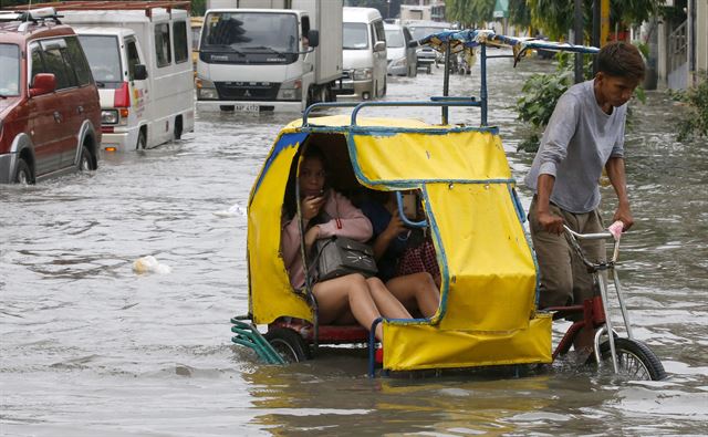 태풍 암필의 영향으로 인한 폭우로 필리핀 마닐라의 저지대가 침수된 가운데 20일(현지시간) 시민들이 패디캡(승객용 3륜 자전거)을 타고 침수된 거리를 이동하고 있다. AP 연합뉴스