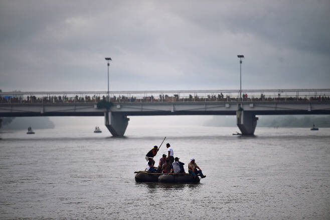 뗏목을 이용해 수치아떼 강을 건너고 있는 온두라스 이민자들 뒤 다리 위에 캐러밴이 보인다. AFP=연합뉴스