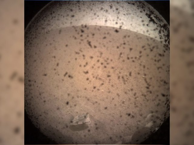 인사이트가 화성의 엘리시움 평원에 안착한 후 최초로 찍어 보낸 착륙 지점 광경. 이미지에 보이는 얼룩들은 먼지가 렌즈 덮개에 엉겨붙어 생긴 것이다. (출처: NASA/JPL-Caltech)