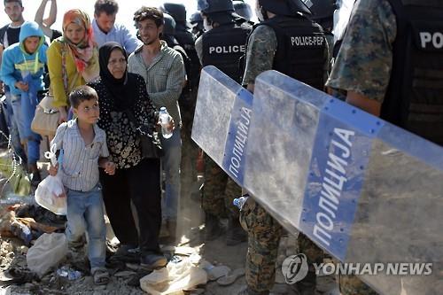 2015년 2월 마케도니아 시위 진압 경찰 옆을 지나는 난민들 [EPA=연합뉴스 자료사진]