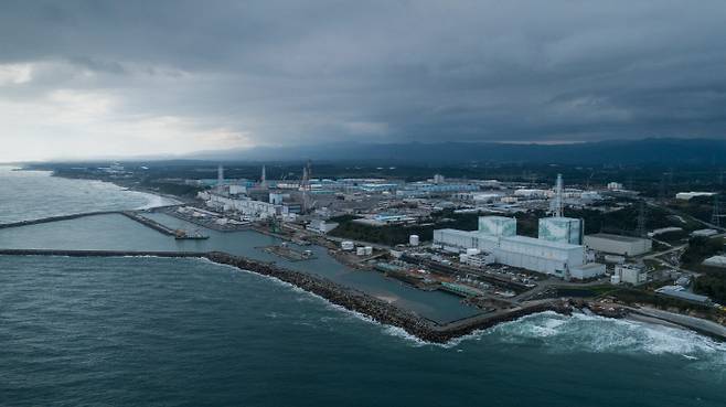 그린피스에서 지난해 10월17일 공중 촬영한 후쿠시마 원전의 모습. 사진 왼쪽(남쪽)에 후쿠시마 원자로 1~4호기가 있고, 오른 쪽(북쪽)에 5~6호기가 자리한다. 서쪽과 남쪽에 자리한 후타바와 오쿠마 마을은 접근을 제한하고 있다. 사진 뒤쪽으로 푸른색 구조물처럼 보이는 방사성 오염수 저장탱크 944개가 줄지어 늘어서 있다.   | 그린피스 제공