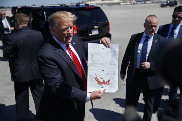 도널드 트럼프 미국 대통령이 22일 전용기 에어포스원으로 미 플로리다주 팜비치 국제공항에 도착한 후 기자들에게 극단주의 무장세력 이슬람국가(IS)의 시리아 내 점령지 격퇴 전후를 비교한 두 지도를 보여주고 있다. 트럼프 대통령은 IS 점령지가 붉은 색으로 넓게 표시된 아래 지도는 2016년 미 대선 전의 것이고 붉은 색이 전혀 없는 위 지도는 현재 모습이라고 밝혔다. 플로리다=AP 연합뉴스