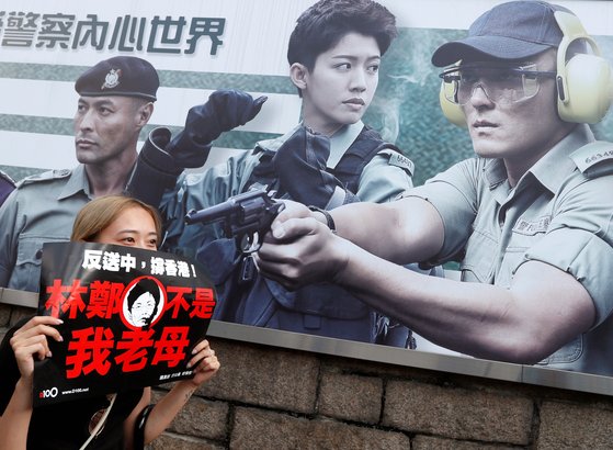 홍콩 경찰 모집 포스터가 붙은 담장 아래서 홍콩의 한 여성이 "캐리 람 행정장관은 더는 우리의 어머니가 아니다"라는 문구가 적힌 플래카드를 들고 있다. [로이터=연합뉴스]