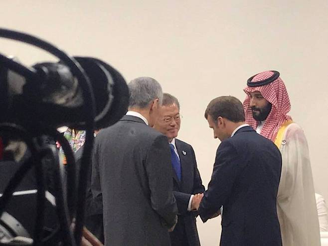 지난 해 프랑스 국빈방문으로 만났던 에마뉘엘 마크롱 대통령이 문재인 대통령과 두 손을 잡은 채 반갑게 인사하고 있다. 지켜보는 왼쪽 뒷 모습은 리센룽 싱가포르 총리, 오른쪽은 모하메드 왕세자. 청와대 제공