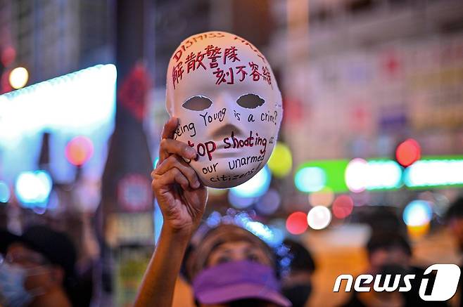지난 10월5일 홍콩 몽콕 경찰서 인근에 시위대가 모이자 한 여성이 시위대의 마스크 착용을 금지하는 복면금지법 시행을 규탄하며 구호가 적힌 마스크를 들고 있다.  © AFP=뉴스1