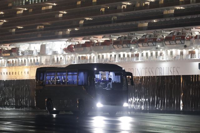 다이아몬드 프린세스 유람선에서 미국 승객을 태운 버스가 17일 월요일 도쿄 인근 요코하마 항구를 출발하고 있다. 버스 뒷편 크루즈에 남겨진 승객들이 버스가 떠나는 모습을 바라보고 있다. AP 연합뉴스
