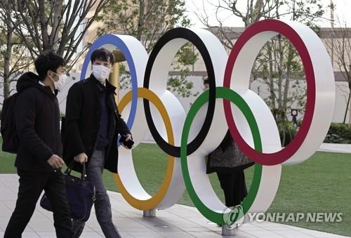 27일(현지시간) 올림픽 상징물 앞을 마스크를 쓴 일본 시민들이 지나가고 있다. [EPA=연합뉴스]