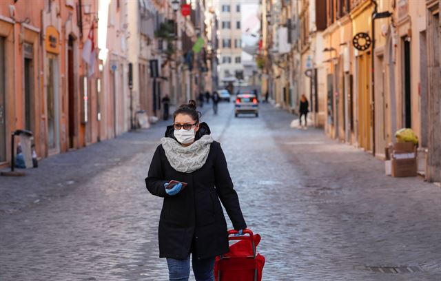 신종 코로나바이러스 감염증(코로나19)이 무서운 속도로 확산하는 이탈리아에서 전례 없는 전국 이동제한령이 발효된 지 사흘째를 맞은 12일(현지시간) 로마에서 한 여성이 마스크를 쓴 채 거의 인적이 끊긴 거리를 지나가고 있다. 로마=로이터 연합뉴스