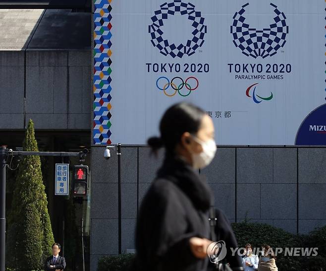 마스크를 쓴 여성이 9일 오후 도쿄 올림픽·패럴림픽 홍보물이 설치된 일본 도쿄도(東京都) 지요다(千代田)구의 한 사거리를 지나는 가운데 근처 신호등에 적신호가 켜져 있다. [연합뉴스 자료사진]