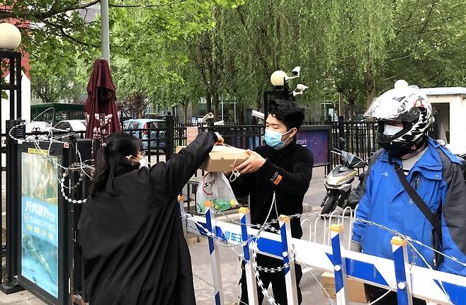 (베이징=연합뉴스) 김윤구 특파원 = 24일 베이징의 한 아파트에서 한 주민이 철조망이 처진 문 너머로 배달 음식을 받고 있다.