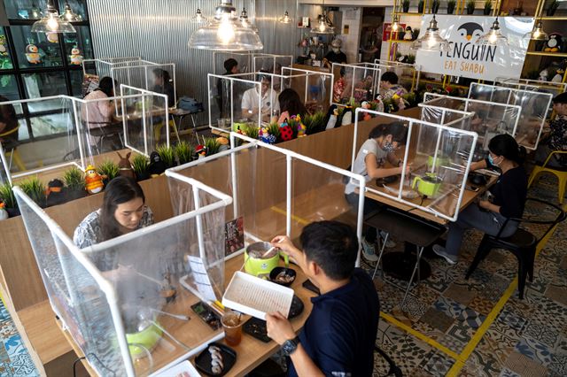 태국 방콕에서 8일 코로나19 확산을 방지하기 위한 조치가 완화되어 영업을 시작한 한 식당을 방문한 시민들이 투명한 칸막이가 설치된 자리에 앉아 음식을 먹고 있다. 방콕=로이터 연합뉴스