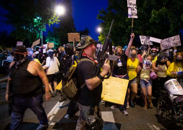 26일 이른 오전 미국 오리건주 포틀랜드에서 노란 옷을 입은 '엄마'들의 호위 속에 시위대가 밤샘 집회를 연 가운데 경찰은 이들을 '폭도'로 규정했다. 포틀랜드=AP 연합뉴스