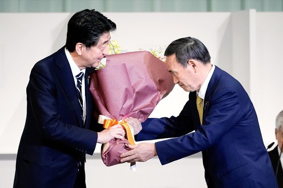 아베 신조 일본 총리(왼쪽)가 14일 도쿄에서 열린 자민당 총재 선거에서 새 총재에 선출돼 사실상 차기 총리로 확정된 스가 요시히데 관방장관에게 꽃다발을 건네고 있다. 로이터=연합뉴스