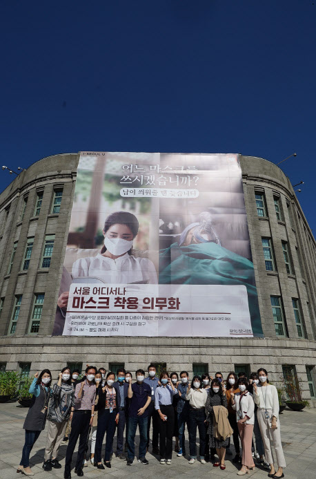서울시 시민소통기획관 부서원들이 서울도서관 외벽에 붙은 ‘마스크 착용 의무화’ 대형 포스터 앞에서 화이팅을 외치고 있다.