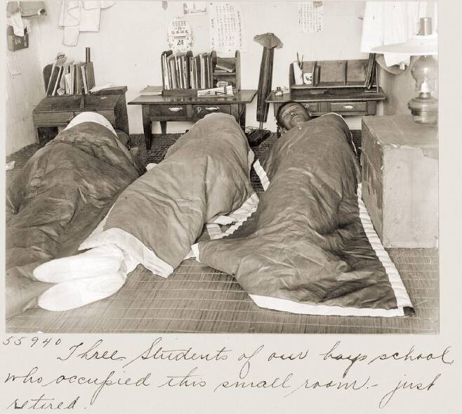 공주 영명학교의 남학생 기숙사 모습, 돗자리가 깔린 작은 방에 책상 3개가 놓여 있고 학생들이 버선발로 잠을 자고 있다.