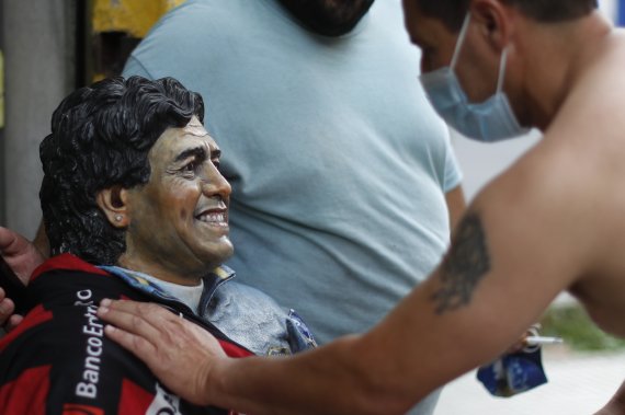 축구전설 디에고 마라도나가 25일(현지시간) 사망한 뒤 아르헨티나 부에노스아이레스의 마라도나 자택 인근 주민이 그의 동상에 손을 올려 애도하고 있다. 사진=AP뉴시스