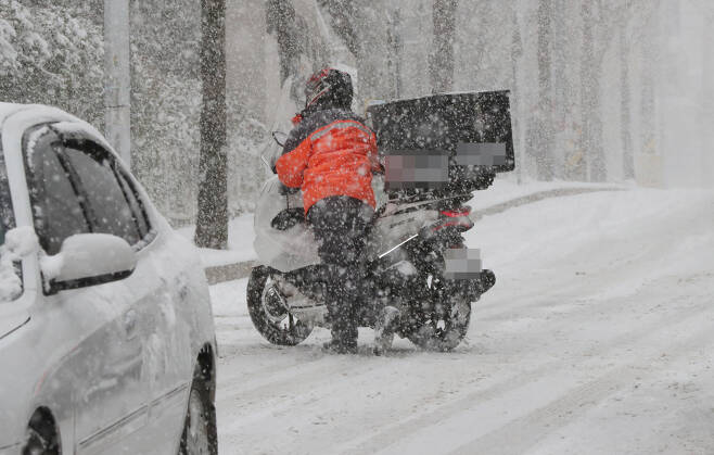 눈이 내린 도로에서 배달 이륜차 운전자가 미끄러운 길에 주행을 멈추고 오토바이를 끌고 가고 있다. [연합뉴스]
