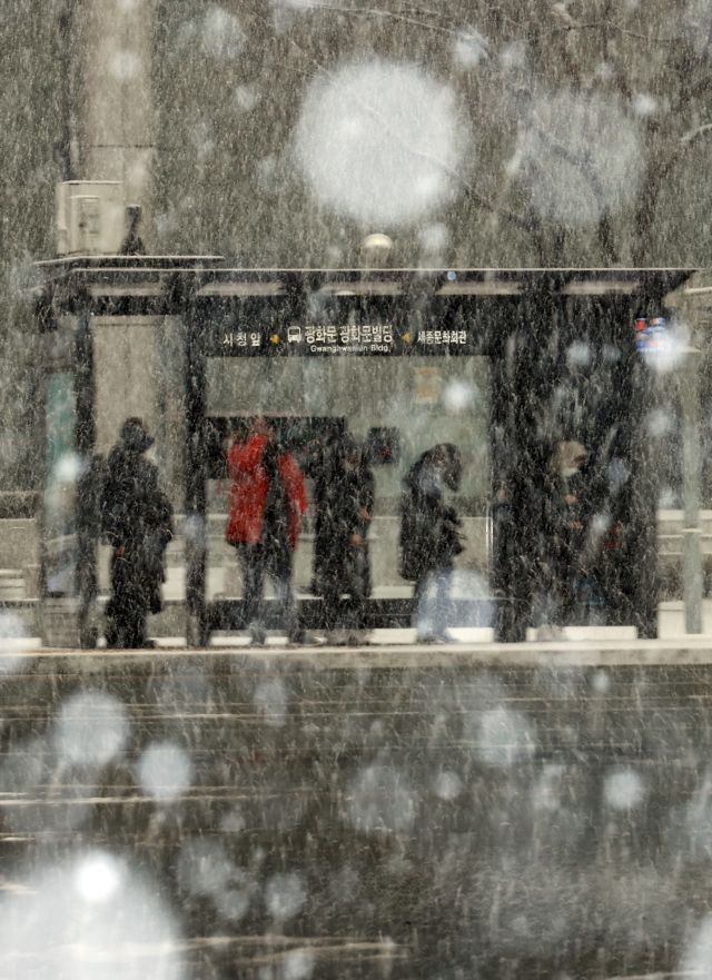 오후 들어 서울 지역에 눈이 내리기 시작한 12일 오후 서울 세종대로의 한 버스정류장에서 시민들이 눈을 맞으며 버스를 기다리고 있다. 연합뉴스