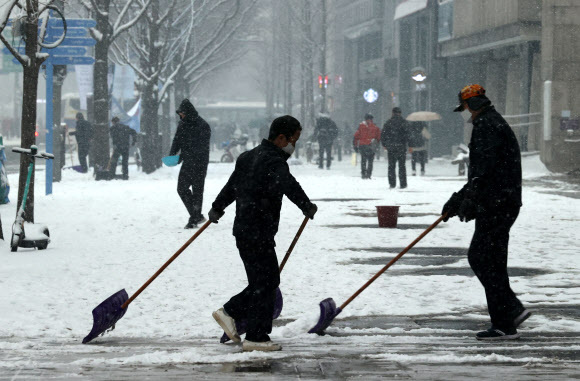 서울 지역에 눈이 내린 12일 오후 서울 종로구 세종문화회관 앞에서 작업자들이 눈을 치우고 있다. 연합뉴스