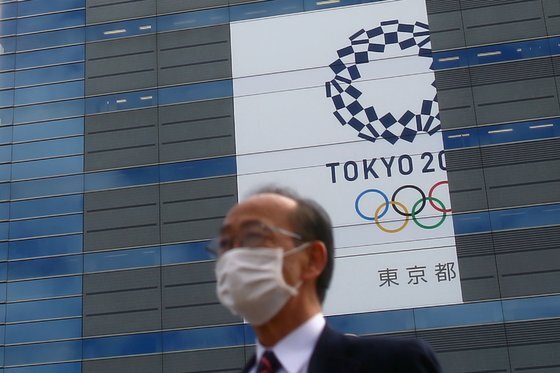 지난해 3월 마스크를 쓴 채 도쿄올림픽 배너 앞을 지나는 도쿄 시민. 로이터=연합뉴스