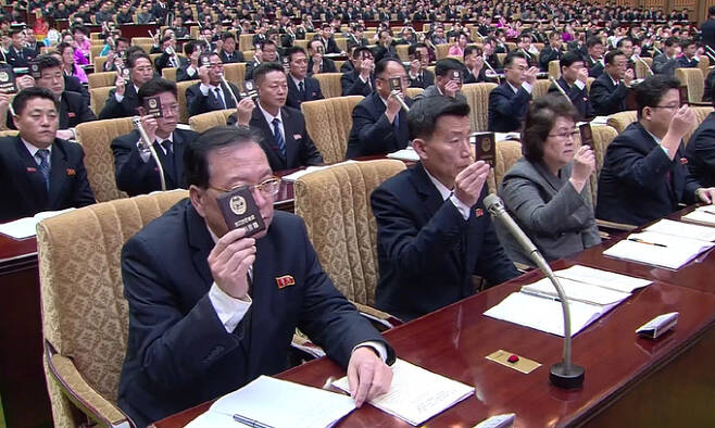 북한 조선중앙TV가 18일 최고인민회의가 전날 개최됐다고 보도했다. 사진은 회의에 참석한 대의원들이 자리에 착석한 채 대의원증을 들어 올리는 모습. 조선중앙TV 캡처·연합뉴스