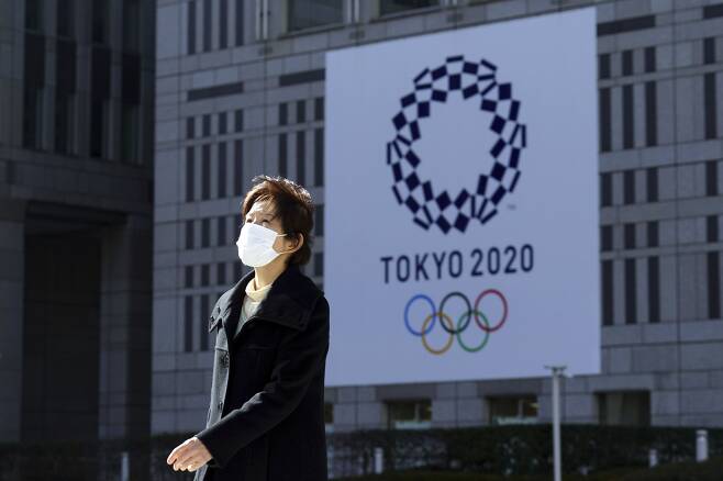 19일(현지 시각) 일본 도쿄에서 한 여성이 마스크를 쓴 채 걷고 있다. 여성의 뒤로는 코로나 팬데믹 여파로 연기된 2020 도쿄올림픽 관련 현수막이 보인다. /AP 연합뉴스
