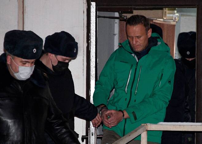 독극물 중독 치료 뒤 독일에서 귀국 직후 체포된 알렉세이 나발니가 지난 18일(현지시간) 30일간 구속하라는 법원의 판결 직후 수갑을 찬 채 경찰의 호위를 받으며 모스크바 외곽 힘키 경찰서 밖으로 나오고 있다. /AFP 연합뉴스