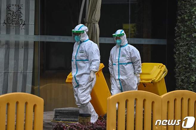 세계보건기구(WHO) 전문가팀이 격리돼 있는 중국 후베이성 우한시 제이드 부티크 호텔에서 전신보호복을 착용한 근로자 2명이 건물 앞을 걸어가고 있다. © AFP=뉴스1