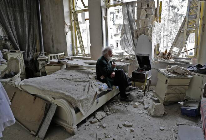 2017년 3월 9일 70세의 아부 오마르가 폭격으로 파괴된 그의 집 침대에 앉아 파이프 담배를 피우며 턴테이블로 음악을 듣고 있다. 반군이 장악했던 알레포 주 알 샤르다. AFP=연합뉴스