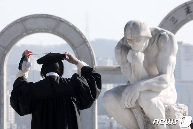 경기도 용인의 한 대학교에서 한 졸업생이 로댕의 '생각하는 사람' 작품 모형을 보며 학사모를 고쳐 쓰고 있다. 2021.2.17/뉴스1 © News1 조태형 기자