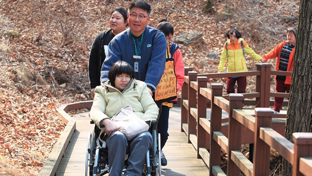 출처: ▶산림치유사가 방문객의 휠체어를 밀며 숲을 설명하고 있는 모습