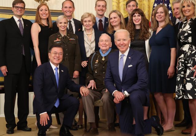 문재인(첫 줄 왼쪽) 대통령과 조 바이든(오른쪽) 미국 대통령이 21일 워싱턴 백악관 이스트룸에서 열린 랠프 퍼켓 주니어(가운데) 예비역 대령 명예훈장 수여식에서 무릎을 꿇은 채 가족과 함께 기념촬영을 하고 있다. 워싱턴=뉴시스