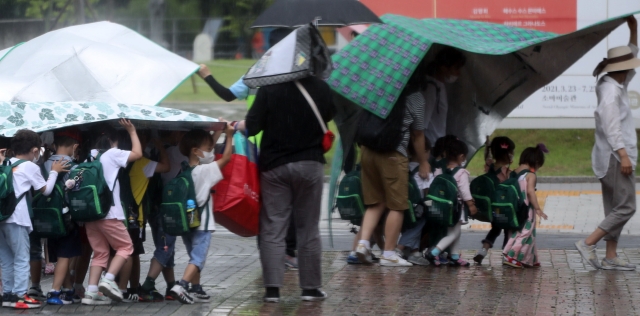 22일 서울 한 공원에서 소나기가 내리자 어린이집 선생님들이 돗자리로 우산을 만들고 있다. 연합뉴스