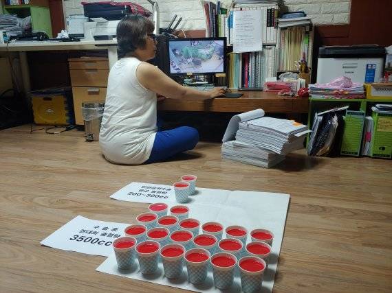수술 중 권대희씨가 흘린 혈액 최소 추정치인 3500cc와 통상적인 안면윤곽수술 실혈량을 비교한 모습. 고 권대희씨 어머니 이나금씨가 권씨의 출혈 심각성을 시각적으로 보이기 위해 종이컵에 붉은 물감을 탄 물을 직접 담았다. 사진=김성호 기자