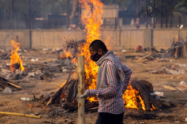 인도 뉴델리의 한 화장터에서 지난 4월 22일(현지시간) 코로나19 사망자들의 시신이 장작불에 타고 있는 가운데 한 남성이 근처를 지나고 있다. 연합뉴스