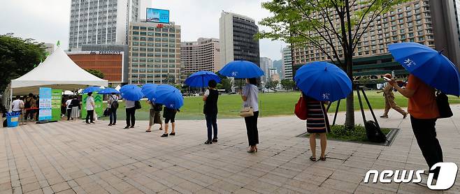 전국 대부분 지역에 폭염특보가 발효된 28일 중구 서울광장에 마련된 코로나19 임시선별검사소에서 갑자기 소나기가 내리자 시민들이 우산을 쓴채 줄 서 있다. 2021.7.28/뉴스1 © News1 안은나 기자