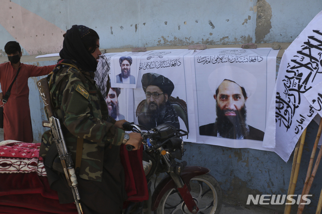 [카불=AP/뉴시스] 25일(현지시간) 아프가니스탄 카불에서 한 탈레반 병사가 탈레반 깃발과 지도자들 사진을 바라보고 있다.  2021.08.26.