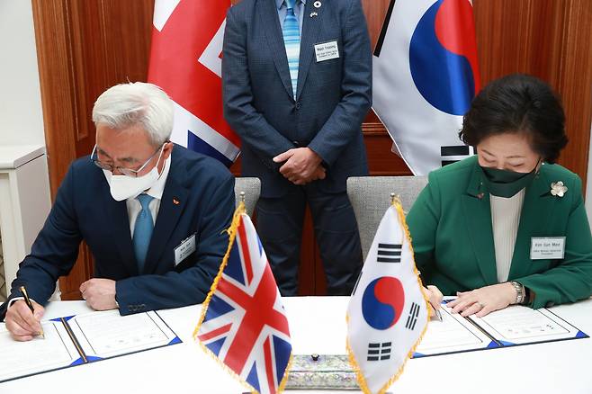 김준 SK이노베이션 총괄사장(왼쪽)과 김은미 이화여대 총장이 13일 주한 영국대사관에서 ‘국제 기후리스크 관리모형 개발’ 협약식을 체결하고, 서명을 하고 있다.[SK이노베이션 제공]